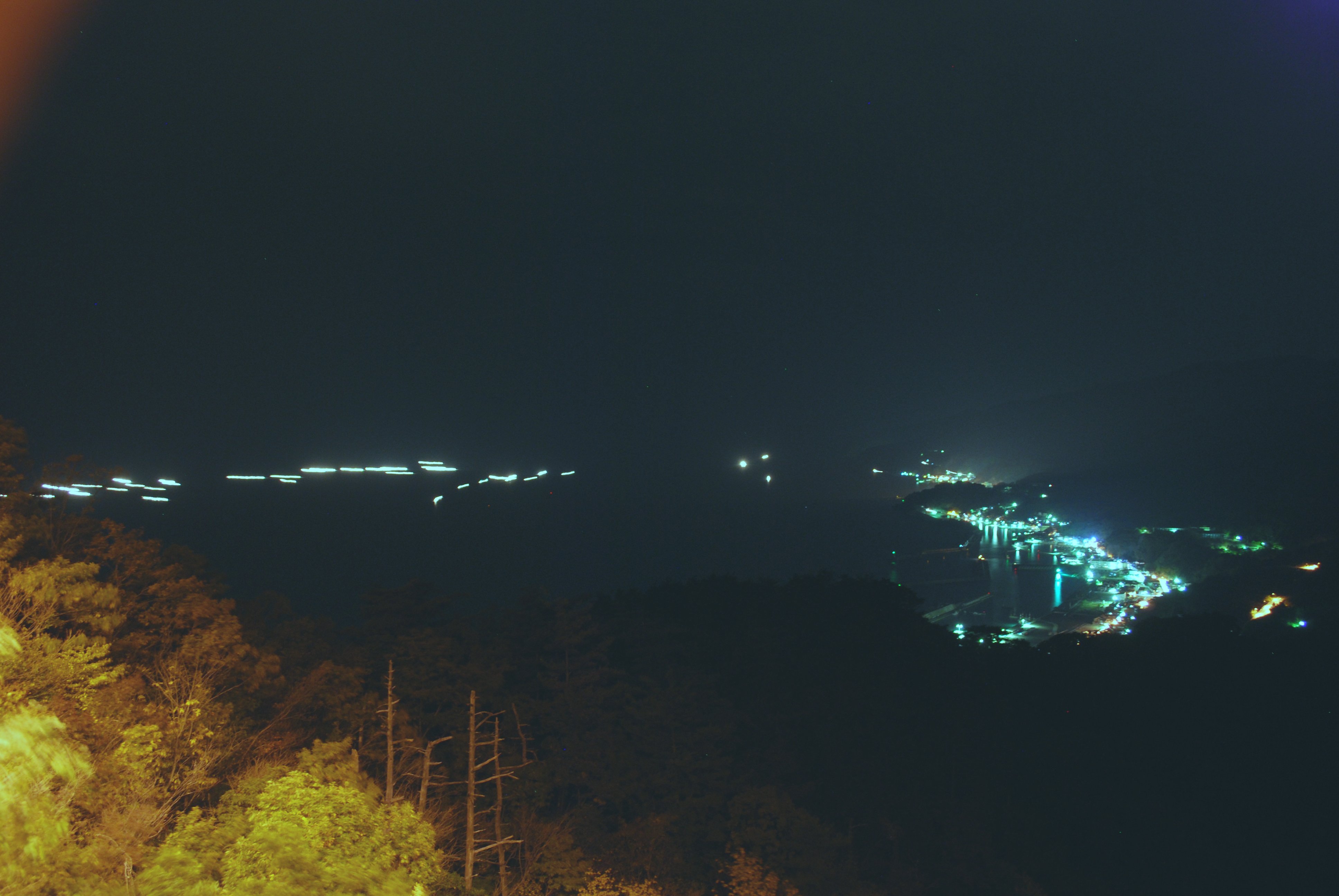 越前がに漁に向け出港する底引き網船の光と港の明かりが幻想的な光景を創り出している＝５日午後１０時４０分ごろ、福井県越前町