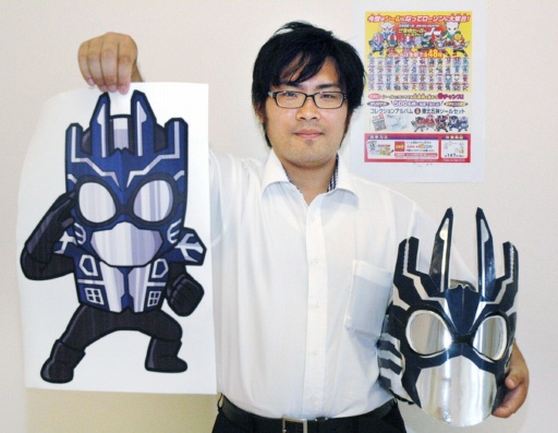 「ゴーイクザー」のマスク（右）と、シールに使ったイラストを持つ諏訪さん＝１２日、福井市内