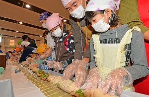 約８０人が参加し、和気あいあいと２９．１メートルの焼き鯖寿司を作る親子連れら＝１６日、福井市の県産業会館