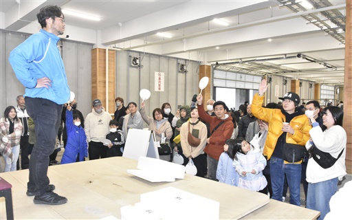 競り体験で、鮮魚や加工品をお得に手に入れようと、うちわを挙げて値段を伝える参加者たち＝１７日、坂井市の三国港市場