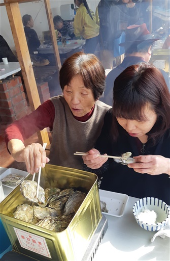 蒸し上がった熱々のカキを味わう来場者＝２月１日、福井県小浜市川崎１丁目のフィッシャーマンズ・ワーフ